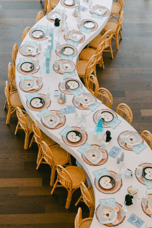 Long, winding dining table set with plates, glasses, and winter-themed decorations for a special...