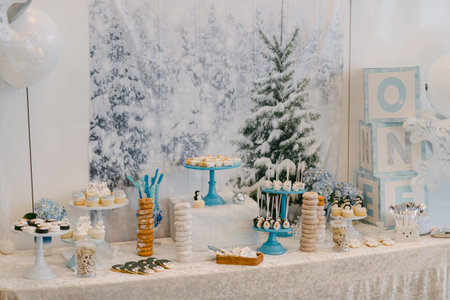 Festive dessert table features sweet treats and decorations for a first birthday celebration in a winter setting.の写真素材