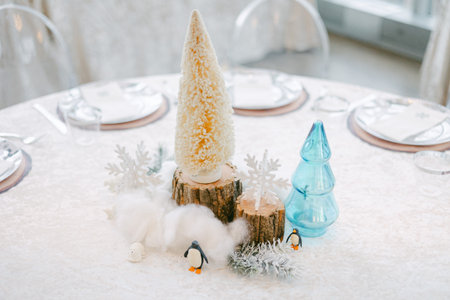 A beautiful winter-themed centerpiece features trees, snowflakes, and small penguins on a dining...