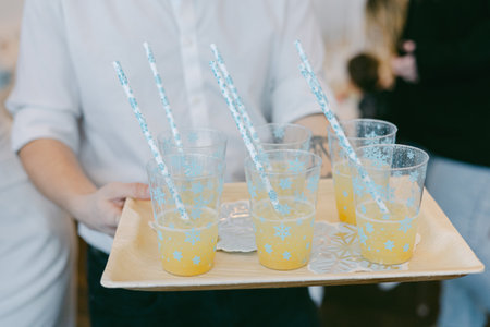 Bright orange drinks served on a tray with festive straws at a joyful celebration indoors, bringing...