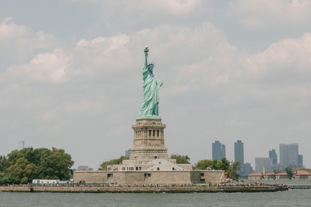Statue of Liberty is seen on Liberty Island under a cloudy sky with the New York City skyline in the...