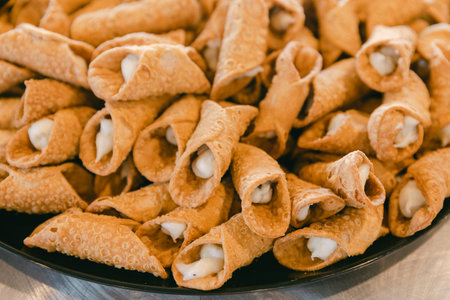 A variety of crispy cannoli stuffed with creamy filling are arranged neatly on a serving platter at...