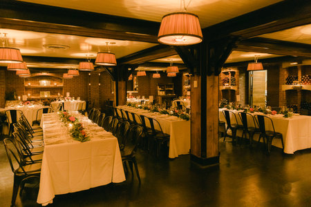 Tables with floral centerpieces await guests in a warmly lit restaurant, perfect for a celebration.