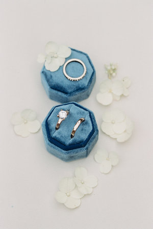 Beautiful rings are arranged on blue velvet with small white flowers, creating a romantic and...
