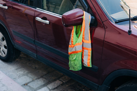 A bright reflective vest drapes over the side mirror of a parked vehicle on a city street in broad daylight.の写真素材
