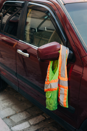 A red vehicle stands parked, displaying a bright safety vest hanging from its side mirror amid city...
