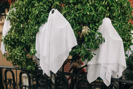 White ghost figures adorn a tree outside a home, creating a festive Halloween atmosphere in the neighborhood.の写真素材