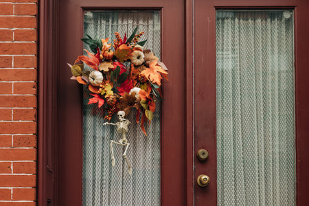 A vibrant wreath made of colorful leaves and flowers hangs on a door with a small skeleton for...