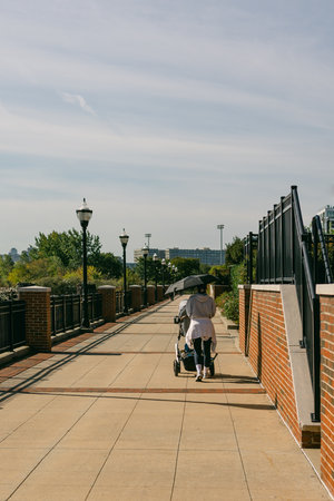 A woman pushes a stroller along a well-maintained path in a park under a clear sky.の写真素材
