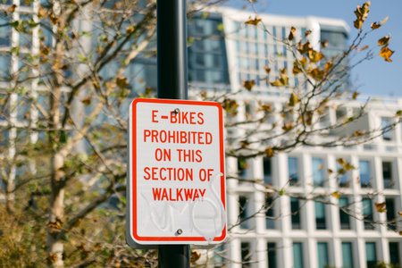 A sign displays that e-bikes are not allowed on a specific walkway surrounded by modern urban buildings.の写真素材
