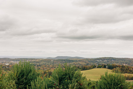 Rolling hills are visible under a cloudy sky with greenery and autumn colors in a peaceful rural...