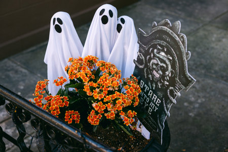 Three ghost decorations are placed among vibrant flowers, creating a festive Halloween scene outside...
