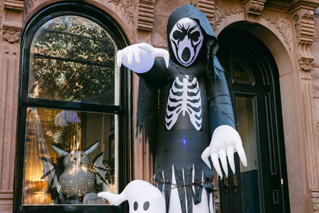 A tall skeleton figure stands outside a brownstone, showcasing festive Halloween vibes in a quaint neighborhood.の写真素材