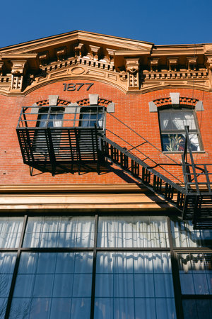 Historic brick structure features a prominent fire escape and intricate designs against a clear blue sky.の写真素材