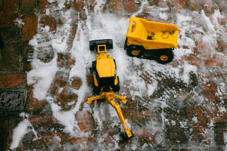Two yellow toy trucks rest on a snowy brick surface, showcasing winter play and creativity on a cold day.の写真素材