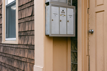 Three mailboxes are fixed to a wall beside a door in a quiet neighborhood, blending with the rustic...