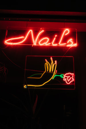 Neon sign at a nails salon shows a hand holding a rose with bright colors illuminating a nighttime scene.の写真素材