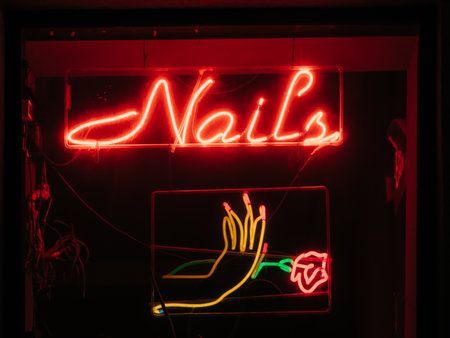 Bright red neon sign clearly displays Nails along with an artistic hand holding a rose against a dark background.の写真素材