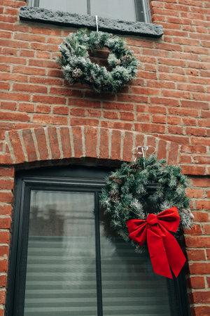 Two beautiful wreaths hang on a brick wall, showcasing winter foliage and red bows for the holiday spirit.の写真素材