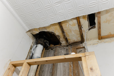 Ceiling damage reveals broken structure and visible pipes during room renovation process.の写真素材