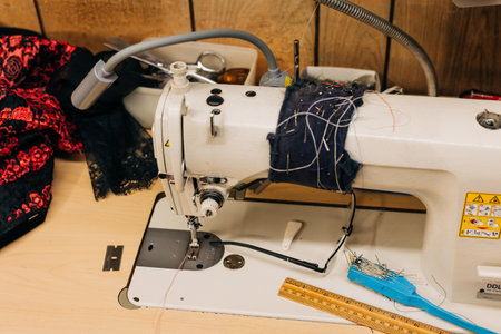 A sewing machine sits on a wooden table surrounded by colorful threads, tools, and fabric scraps in...