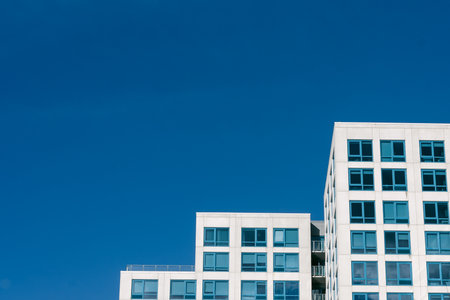Two contemporary buildings rise against a clear blue sky, reflecting sunlight in an urban setting.