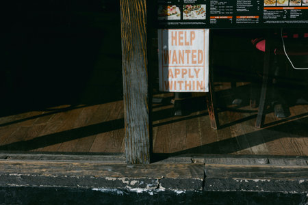 A sign asking for help in a restaurant window invites applicants while sunlight illuminates the scene.の写真素材
