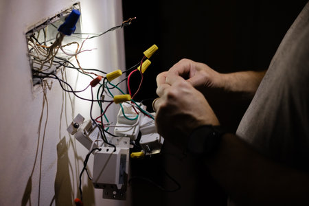 Hands working on electrical wires in a dimly lit room during home repairの写真素材