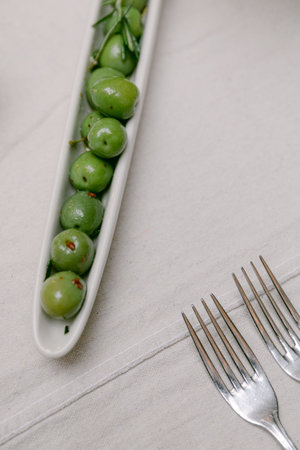 A long dish holds fresh green olives, with two silver forks placed nearby ready for dining.の写真素材