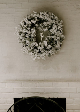 A beautiful frosted wreath hangs above a fireplace in a warm indoor setting, adding a festive touch to the space.の写真素材