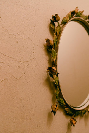 A round mirror adorned with dried flowers hangs on a textured wall, adding charm to the cozy room ambiance.の写真素材