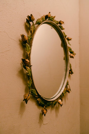 A round mirror decorates a smooth wall, framed with flowers, adding charm to this warm indoor area.
