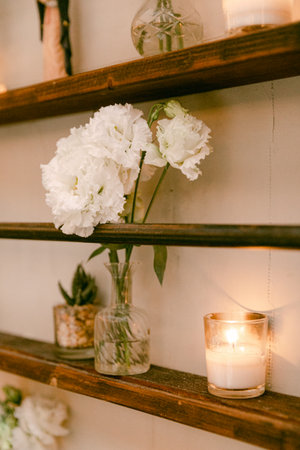A charming display includes white flowers and candles on rustic wooden shelves, creating a warm atmosphere.の写真素材