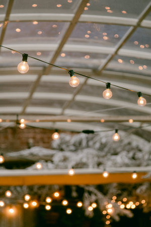 String lights hang above, casting a soft glow under the glass roof, creating a cozy atmosphere during the evening.の写真素材