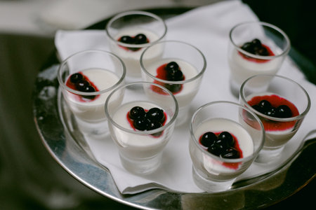 Small cups of panna cotta with blackcurrant sauce and berries served at a stylish gathering.