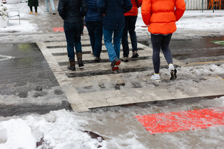 Groups of people walk in the snow, crossing a street while snow falls around them in a winter scene.の写真素材
