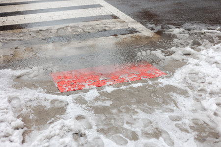 Snow and water on street near crosswalk with a red sign visible around winter timeの写真素材