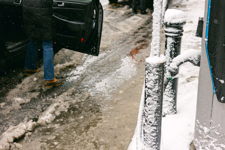 Winter scene with a person getting out of a car on a snowy street near a parking meterの写真素材