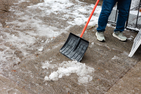 Person shovels snow and ice from a sidewalk in a winter setting during the day in a residential areaの写真素材