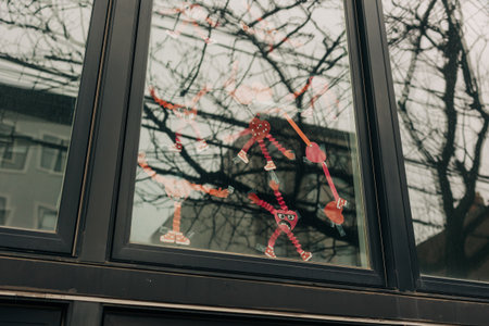 Paper art made by children hangs on a window, showcasing bright colors against a gray sky.
