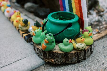 Colorful ducks are lined up on wooden surface by a green pot and rainbow fabric in a bright outdoor...