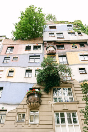 People walk past a colorful building with balconies and greenery in a busy urban setting during the summer.の写真素材