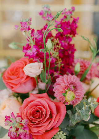 A flower arrangement is placed on a table showcasing roses, stock flowers, and greenery under warm...