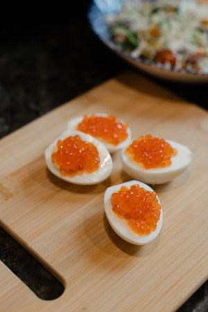 Eggs are cut in half and placed on a wooden board with salmon roe on top.の写真素材