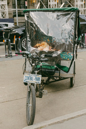 A cyclist stands by a bike cart that is bright and covered near Central Park while cars pass by.の写真素材