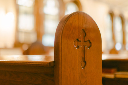 A wooden church pew shows a cross carving in a house of worship filled with soft light during the...