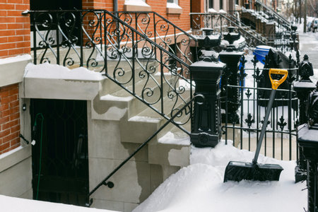 A layer of snow blankets the steps and sidewalk next to a city building after a snowstorm, with a...