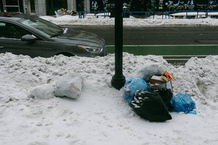 Garbage bags sit on top of snow piles next to a parked car on a busy city street during winter.の写真素材