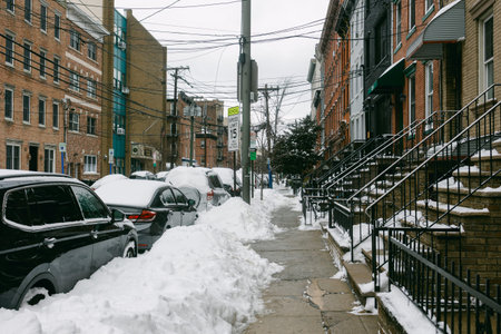 Snow piles up on the sidewalk and cars along the street in a city of Hoboken, NJ, USA during winter, with power lines visible above.の写真素材