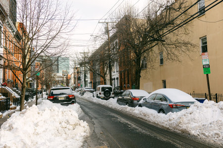 Several cars are parked along a street filled with snow and large snow piles after a winter storm in the city of Hoboken.の写真素材